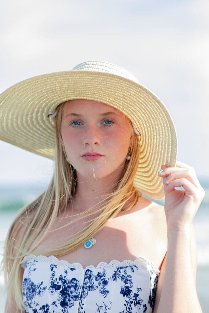 Woman in a summer hat during a Boston beach portrait session, standing by the ocean with coastal breeze.