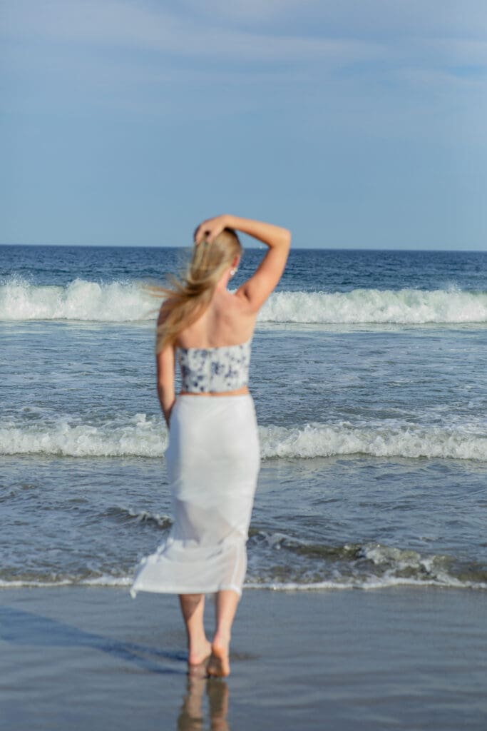 Boston area beach portrait session featuring woman standing at the water’s edge with waves and coastal breeze.