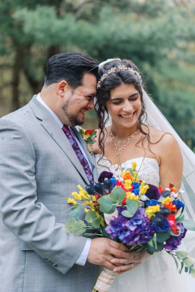 Close-up of a happy bride and groom sharing a candid moment with a colorful bouquet on their wedding day.